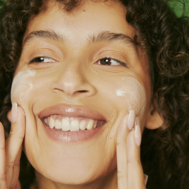 Happy woman spreading cream on cheeks